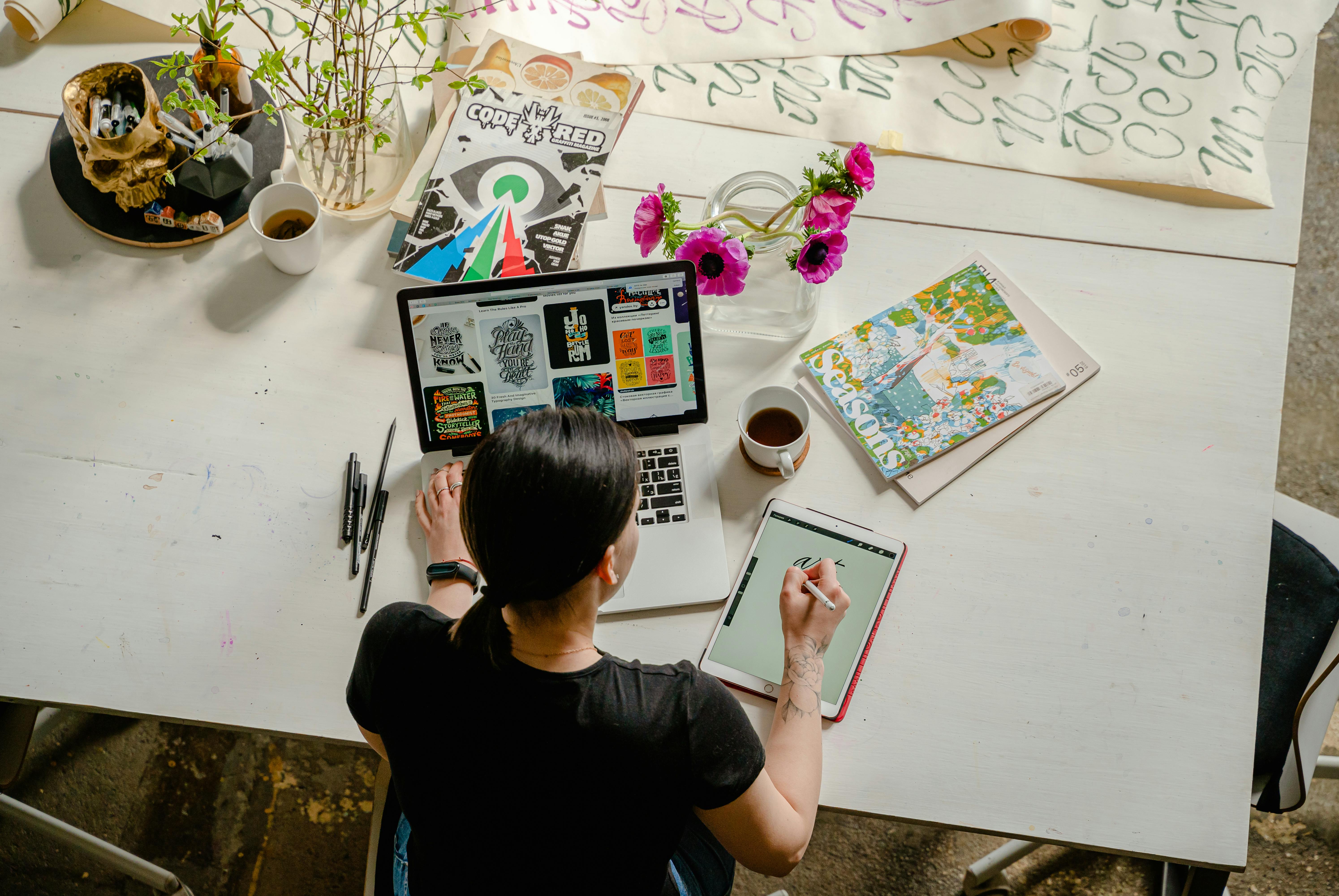Ilustrator, ilustratorica, sjedi za radnim stolom, crta i radi na laptopu