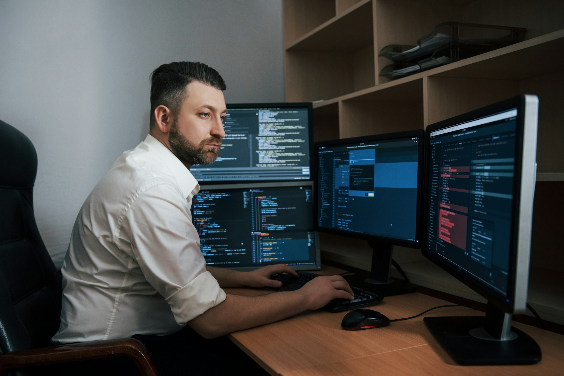 Cybersecurity stručnjak sjedi za stolom  ispred četiri ekrana, tipka na tipkovnicu, pored koje je miš
